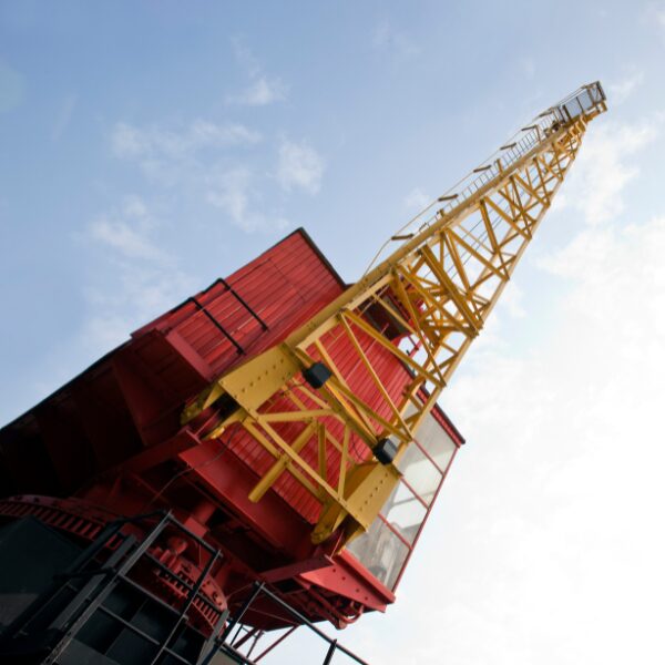A red and yellow tower crane extending into the sky with its boom angled upward.