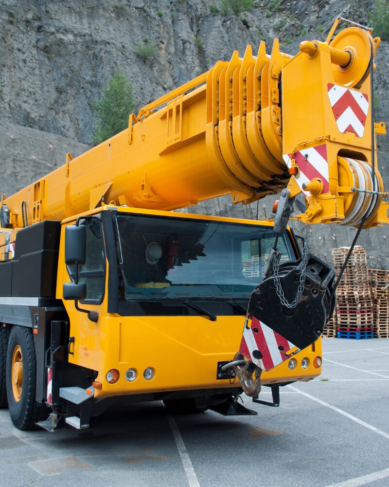 A mobile crane with a yellow telescopic boom parked near a rocky cliff.
